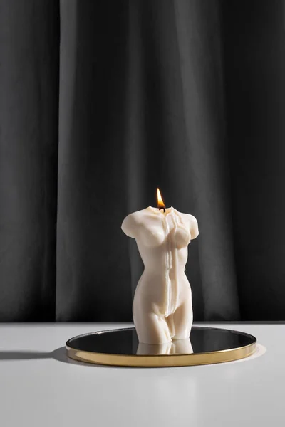 Candle in woman torso shape burning in grey modern interior room, atmosphere and smoke after candle