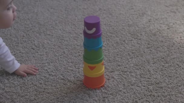 Un bambino di un anno che gioca con giocattoli educativi a casa. Il bambino con gli occhi azzurri sta giocando con il giocattolo della piramide sul pavimento. Ragazzino divertirsi in casa — Video Stock