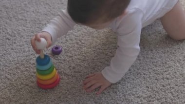 Evde eğitim kupası oyuncaklarıyla oynayan bir yaşında bir çocuk. Mavi gözlü küçük bebek yerde piramit oyuncağıyla oynuyor. Küçük çocuk içeride iyi eğlenceler.
