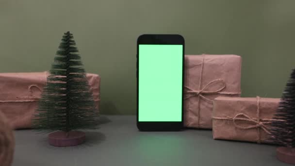 Mobiltelefon in vertikaler Ausrichtung mit grünem Bildschirm auf einem Hintergrund von Weihnachtsbaum und Geschenk in Handwerk. Online-Shop, App-Promo, Anzeigen. Zoom in Schuss — Stockvideo