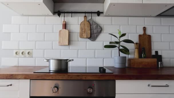 Utensílios de cozinha de latão, acessórios de cozinha.Água ferve em uma panela. Cozinha pendurada com azulejos brancos parede e mesa de madeira.Planta verde no fundo da cozinha — Vídeo de Stock