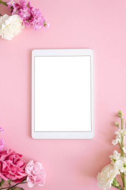 Pembe arkaplan çiçekleri üzerine beyaz ekranlı iPad pro tablet. Ofis tasarımcısı kadın geçmişi
