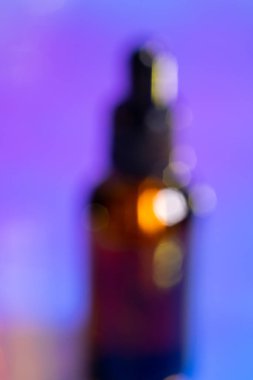 Pembe ve mor arka planda pipeti olan cam şişede bulanık yağlı serum, fotokopi alanı olan neon ışığı. Modern ve gelecekçi kozmetik