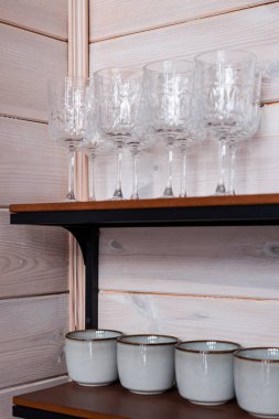Ahşap bir rafta temiz cam eşyalar. Şarap kadehleri ahşap bir arka planda rafta duruyor. Güzel bir evde dekor olarak kullanılan aletler..