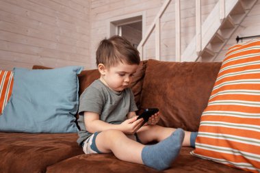 Mutlu küçük çocuk cep telefonunda eğleniyor, küçük çocuk kanepede oturuyor akıllı telefonda çizgi film izliyor, çocuk evde dinlenirken cep telefonu kullanıyor.