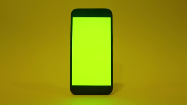 緑の画面で携帯電話のiPhone 13 、スマートフォンのモックアップ。緑と黄色の照明。フラットスクリーン現代的なスマートフォン — ストック動画