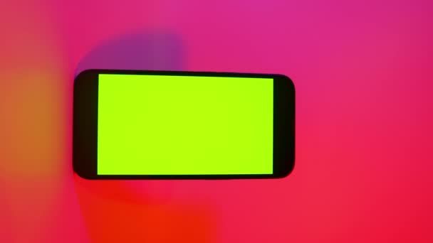 Cellulare iPhone 13 con schermo verde, smartphone mock up. Illuminazione di colore rosa e viola. Smartphone moderno a schermo piatto — Video Stock