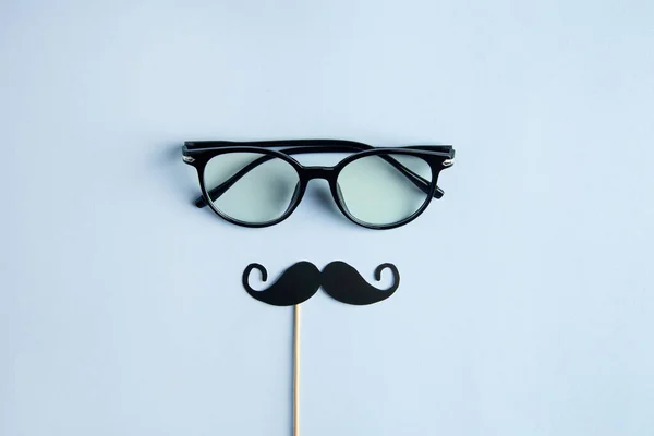 Día de los Padres Concepto de vacaciones. Gafas transparentes, elegante cabina de fotos de papel negro con bigotes sobre fondo azul. — Foto de Stock