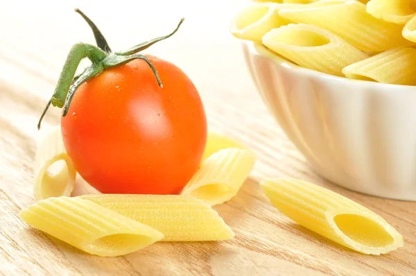 Several uncooked penne pasta and a cherry tomato, closeup — Stock Photo, Image