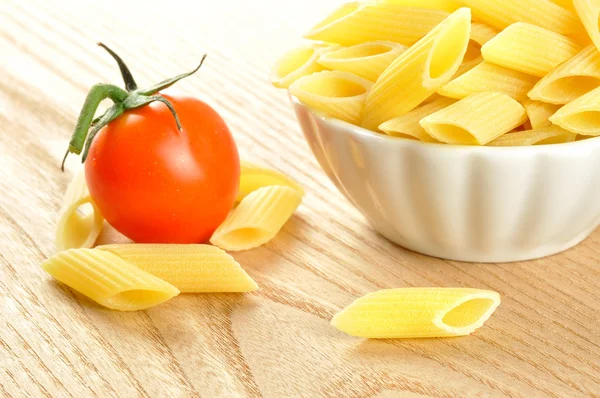 Several uncooked penne pasta and a cherry tomato, closeup — Stock Photo, Image