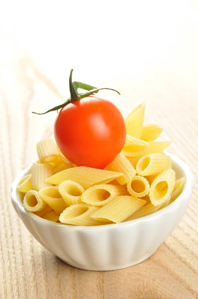 Several uncooked penne pasta and a cherry tomato in a small bowl — Stock Photo, Image