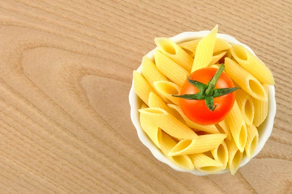 Several uncooked penne pasta and a cherry tomato in a small bowl — Stock Photo, Image