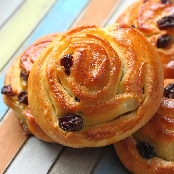 Fresh sweet swirl buns with raisins on colored wooden table — Stock Photo, Image