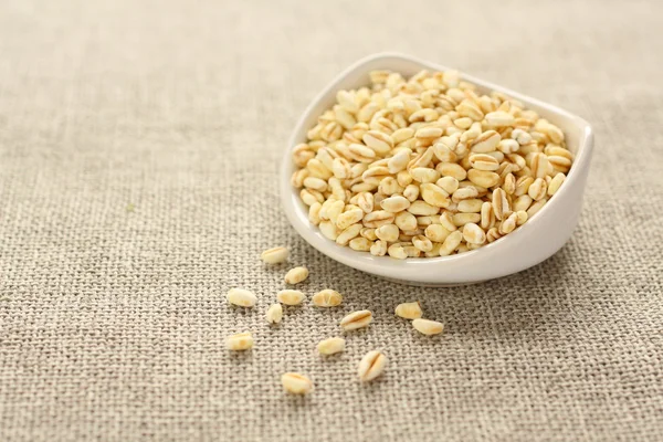 Wheat grains in white ceramic bowl on sackcloth background — Stock Photo, Image