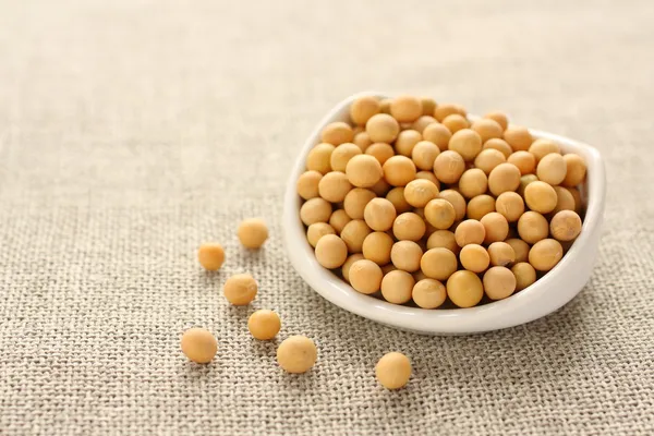 Soybeans in white ceramic bowl on sackcloth background — Stock Photo, Image