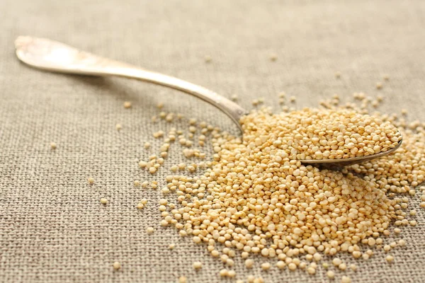 Quinoa grain in metal spoon on sackcloth background — Stock Photo, Image