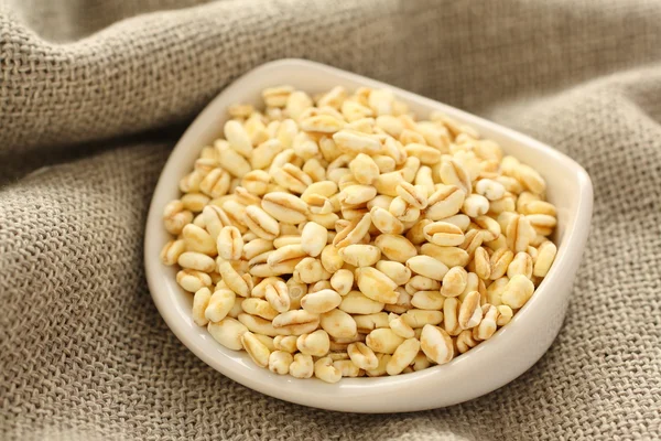 Pšeničná zrna v bílé keramické misky na pozadí pytloviny — Stock fotografie