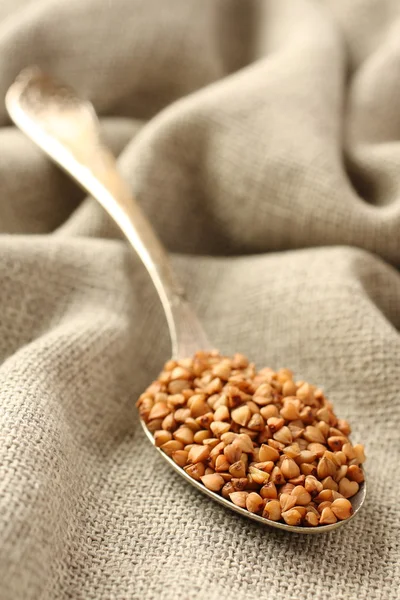 Buckwheat grains in metal spoon on sackcloth background — Stock Photo, Image