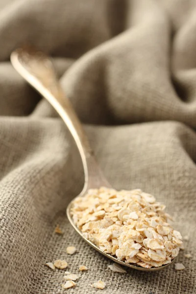 Oat flakes in metal spoon on sackcloth background — Stock Photo, Image