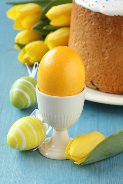 Kleurrijke paaseieren, brood en gele tulpen op blauwe houten achtergrond — Stockfoto