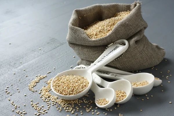 Quinoa grain in small burlap sack and porcelain measuring spoons — Stock Photo, Image