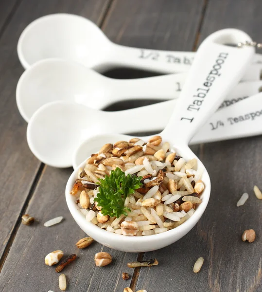 Uncooked multigrain rice in porcelain measuring spoons on wooden background — Stock Photo, Image