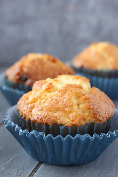 Muffin con uvetta in involucri blu su fondo rustico in legno — Foto Stock