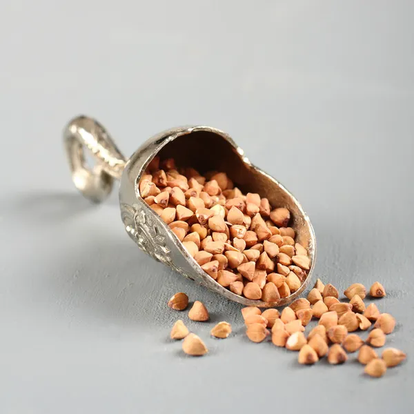Colher de metal com grão de trigo sarraceno no fundo cinza — Fotografia de Stock