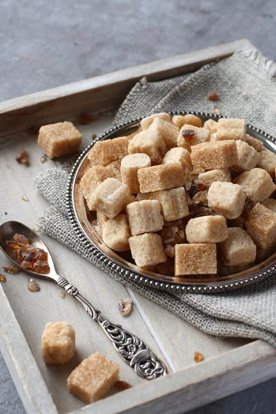 Heap of brown sugar cubes on metal plate on wooden tray — Stock Photo, Image