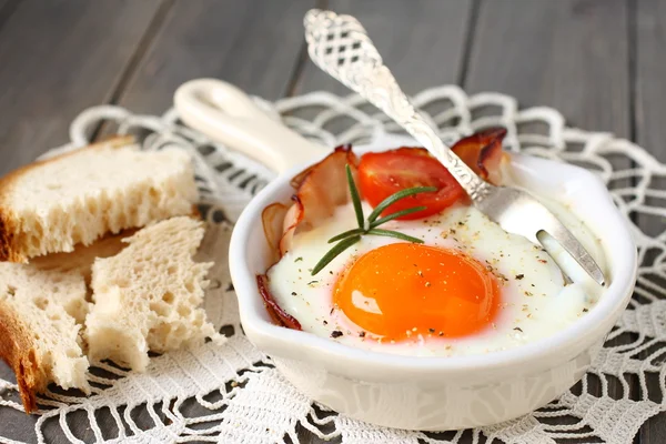 Fried egg with bacon, tomato and rosemary on wooden background — Stock Photo, Image