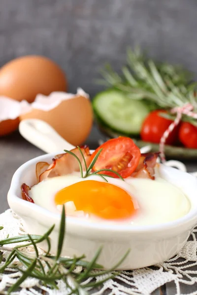 Fried egg with bacon in ceramic pan on wooden background