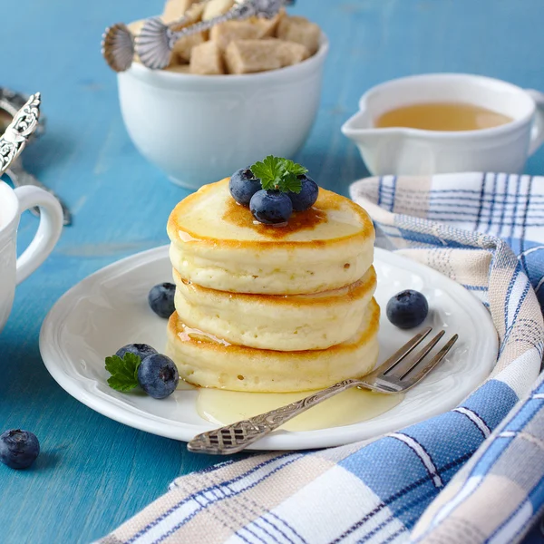 A stack of scotch pancakes with with honey and blueberries on a breakfast table — Stock Photo, Image