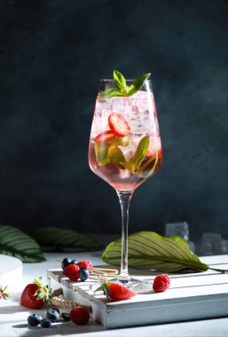 Menü barı. İçkiler ve kokteyller. Buzlu, dutlu, meyveli ve naneli alkollü içecek. Beyaz bir masada çilek, yabanmersini, ahududu ve yeşil yapraklar. Arkaplan resmi, alanı kopyala