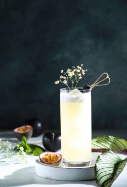 İçkiler ve kokteyller. Tutku meyvesi, erik ve buzlu alkollü sarı kokteyl. Güneş ışığı, yaz, çiçekler. Tropikal konsept. Yeşil yapraklar. Arkaplan resmi, kopyalama alanı, çubuk menüsü