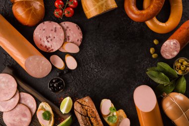 Sosis ve et lezzetleri. Dilimlenmiş jambon, sandviç, zeytin, baget, siyah arka planda baharatlı siyah ekmek. Arkaplan resmi, kopyalama alanı, düz alan, üst görünüm