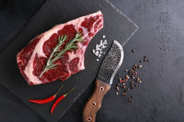 Çiğ et. Kara tahtada biftek, baharat, biberiye, kırmızı biber, siyah masada bıçak. Arkaplan resmi, kopyalama alanı, düz alan, üst görünüm