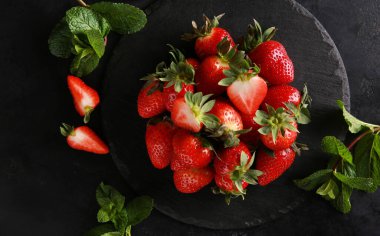 Fresh berry. Red strawberries with green leaves and mint on a black table. Background image, copy space, flatlay, top view