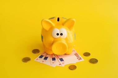 Domuz kumbarası, para sikkeleri ve sarı arka planda euro banknotları. Tasarruf finansmanı krediler para değişimi