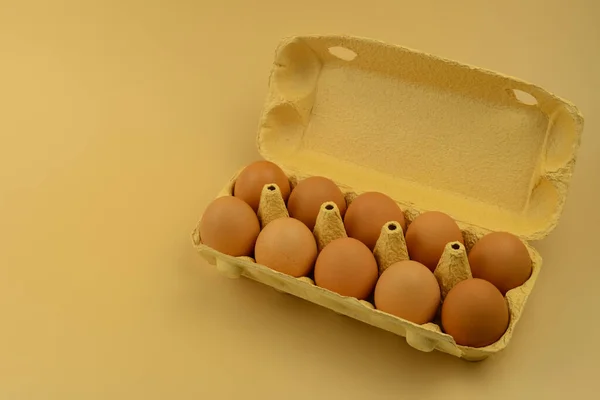 Ten eggs in an open cardboard box on a beige background, copy space. Farm hen eggs box. Healthy food