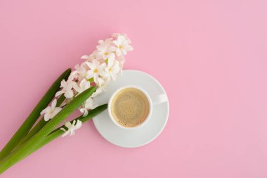 Pembe masanın üstünde bir fincan kahve ve bahar çiçeği, üst manzara. Espresso, pembe pastel arka planda çiçekler.