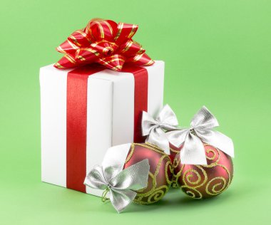Kırmızı kurdeleli beyaz hediye kutusu ve Noel topları.