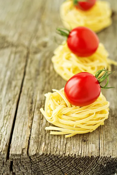 Nidos de pasta con tomates cherry sobre un fondo de madera — Foto de Stock