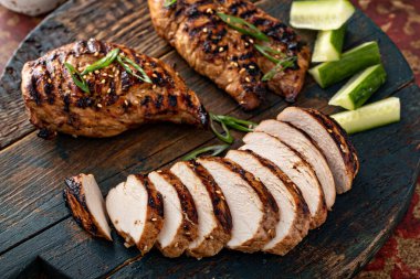 Izgara teriyaki tavuk göğsü yeşil soğanlı bir tahtada dilimlenmiş.