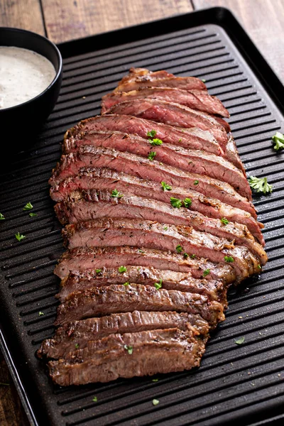 Grilled flank steak with horseradish sauce on a grill pan on wooden table