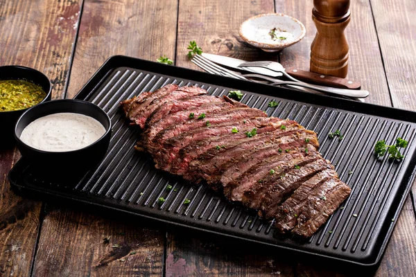 Grilled flank steak with chimichurri and horseradish sauce on a grill pan on wooden table