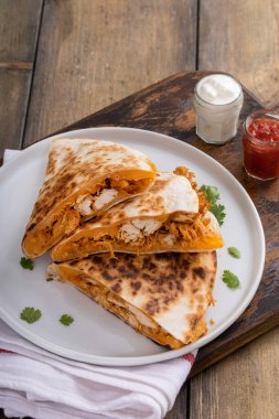 Çedar ve tavuklu quesadilla ekşi krema ve salsa sosuyla servis edilen bir tabakta dilimlenmiş.