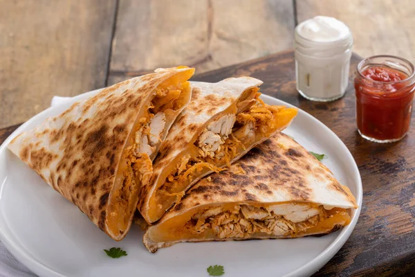Çedar ve tavuklu quesadilla ekşi krema ve salsa sosuyla servis edilen bir tabakta dilimlenmiş.