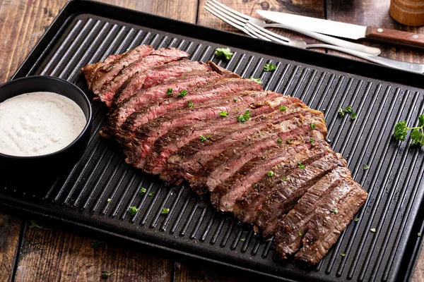 Grilled flank steak with horseradish sauce on a grill pan on wooden table