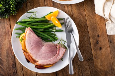 Christmas or Thanksgiving spiral sliced ham with oranges and herbs, served on a plate with green beans