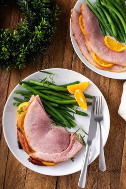 Christmas or Thanksgiving spiral sliced ham with oranges and herbs, served on a plate with green beans